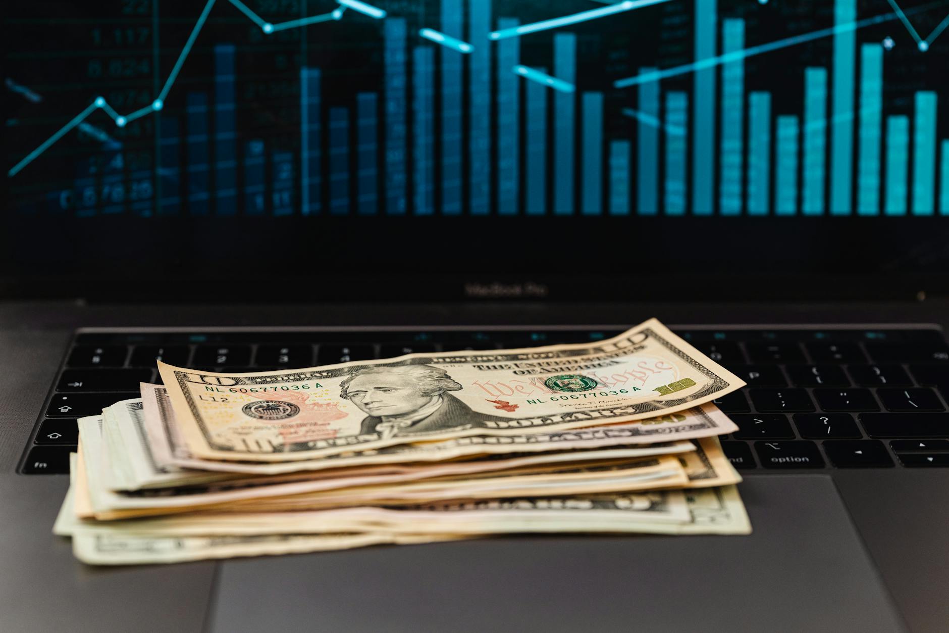 Banknoty dolarowe na laptopie z wykresem finansowym w tle