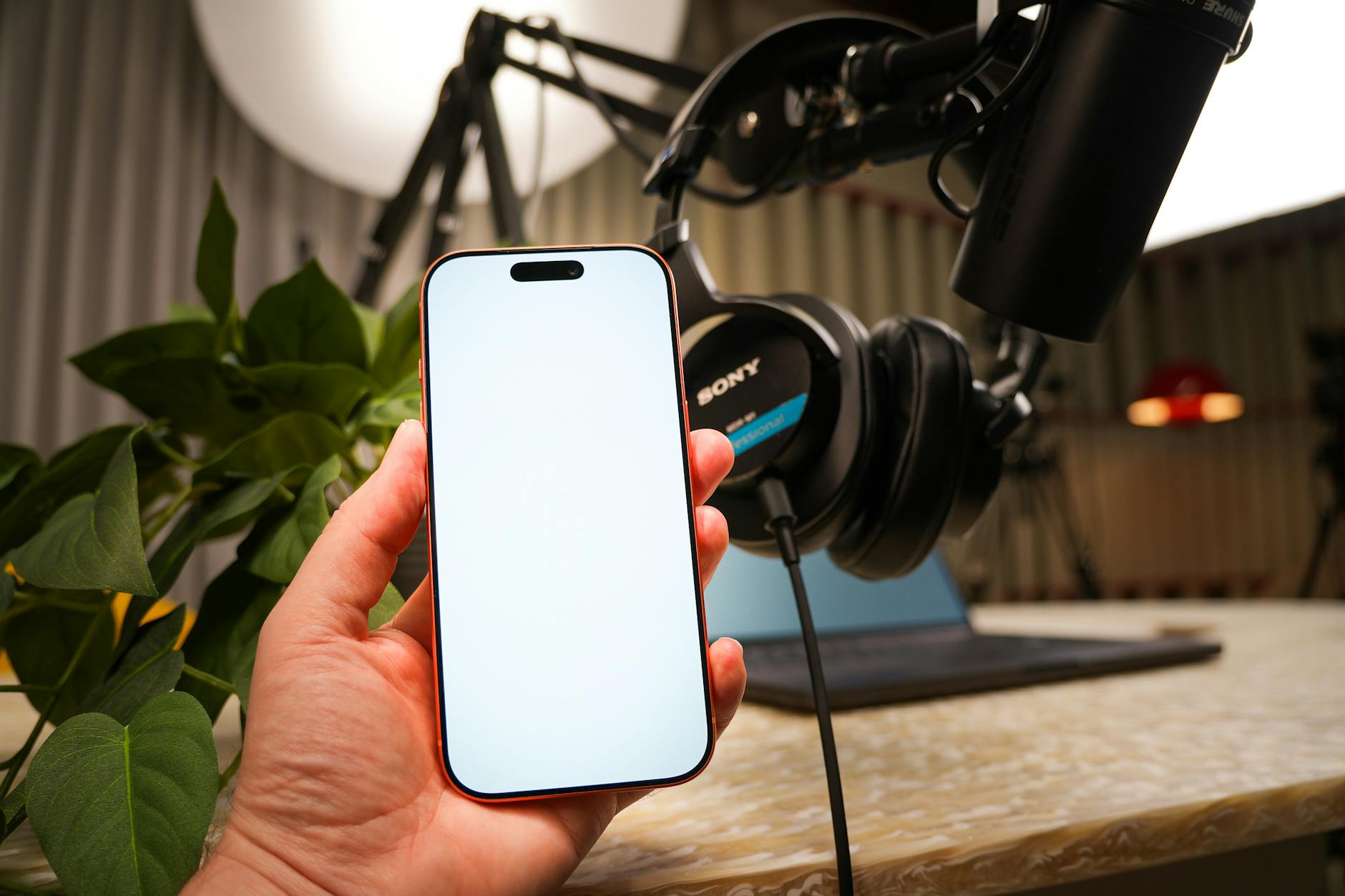 Dłoń z smartfonem w domowym studio nagraniowym z mikrofonem i słuchawkami