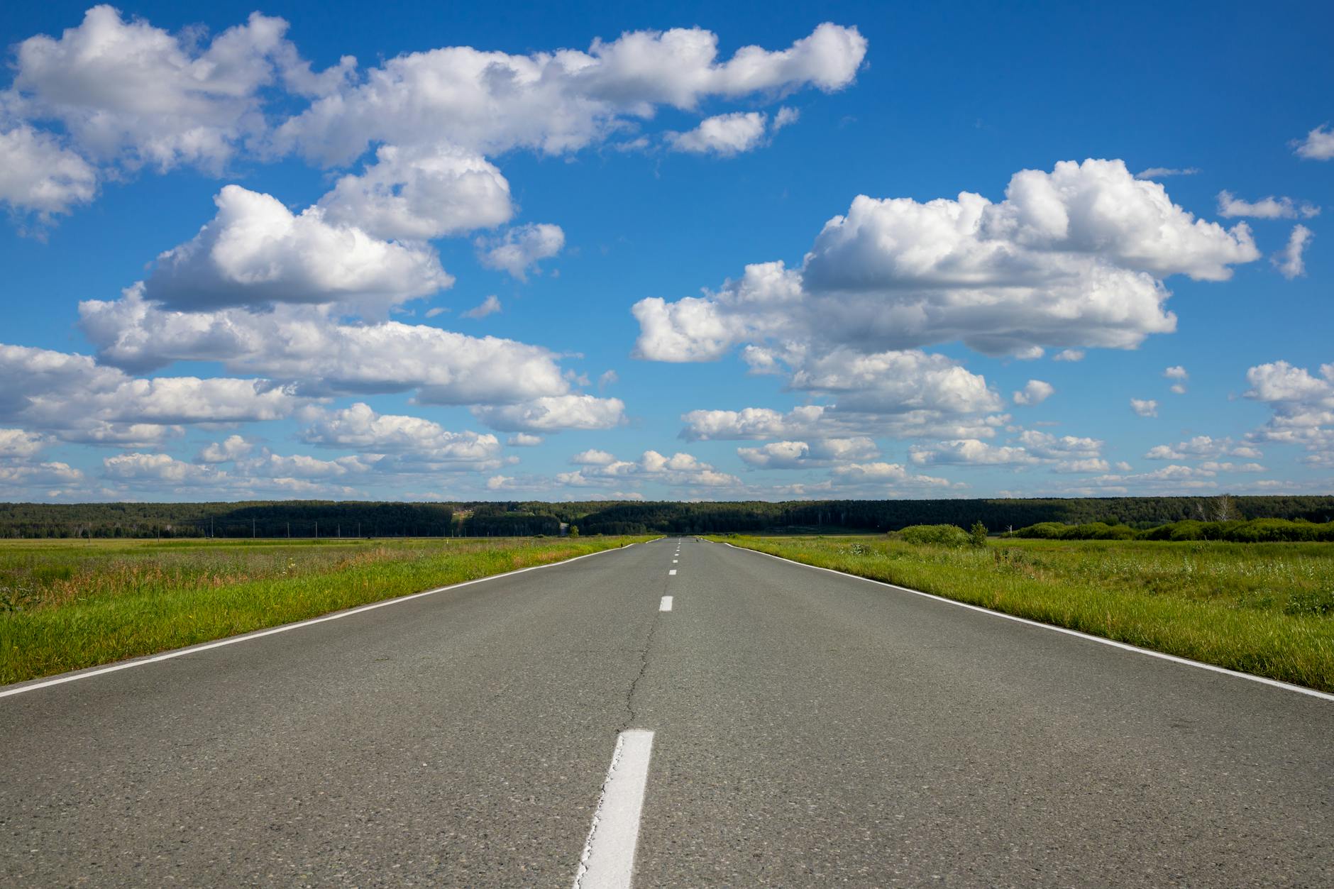 Prosta wiejska droga prowadząca w dal pod błękitnym niebem z chmurami